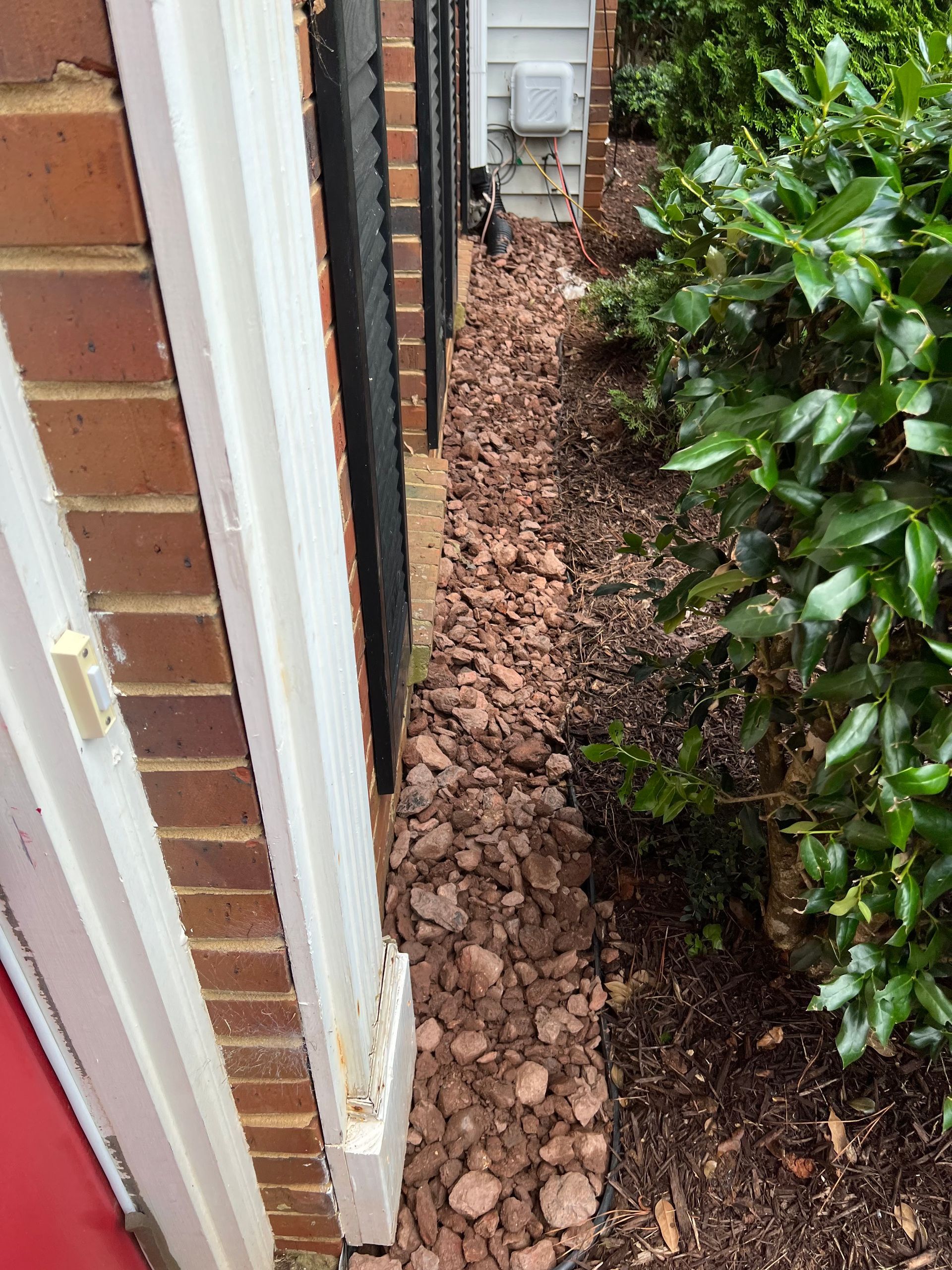Narrow side yard between brick wall and shrubs with mulch piled along the base of the house