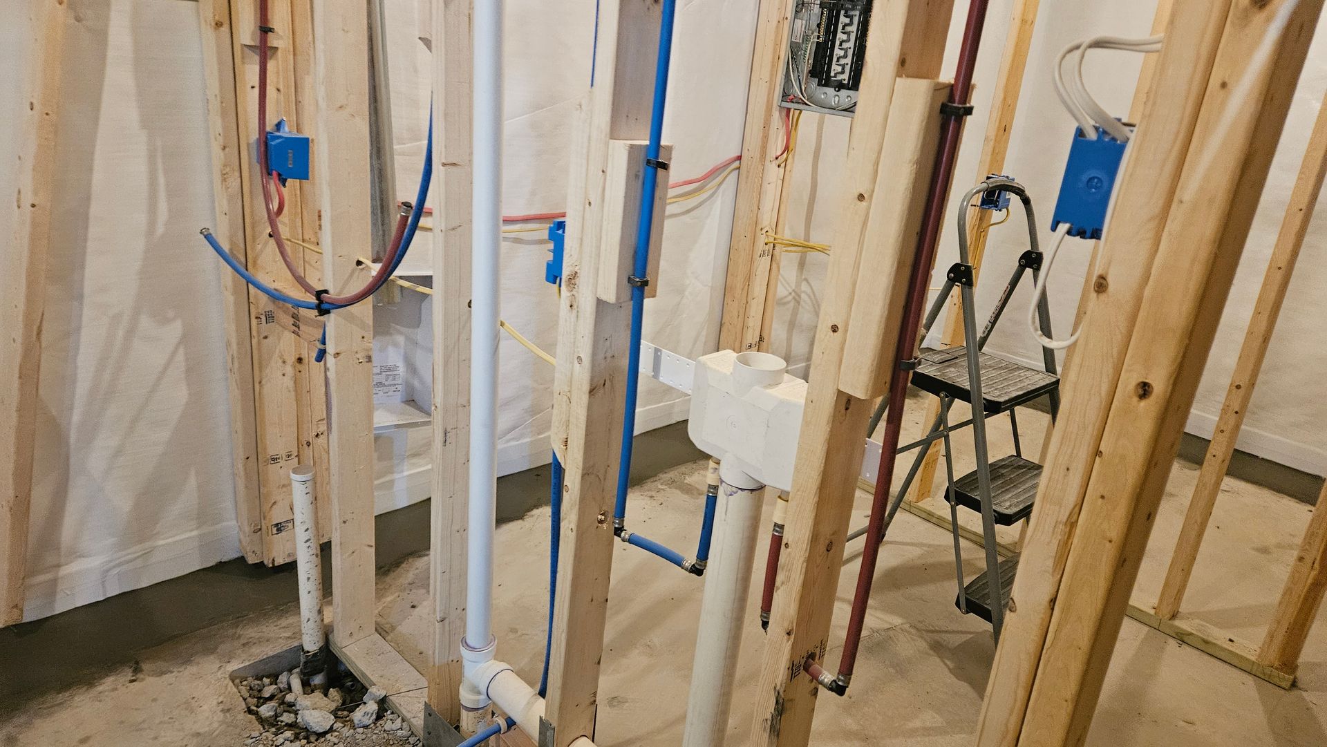 Framed walls and plumbing pipes in a house under construction, with blue tool boxes and wiring.