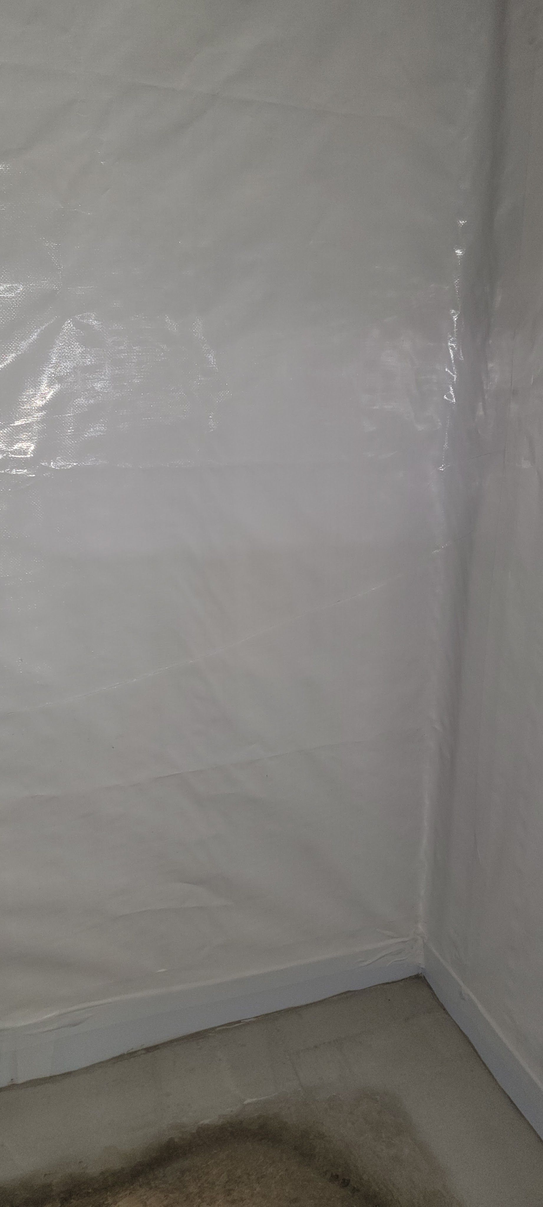 Empty white corner with a plastic-covered wall and gray floor trim.