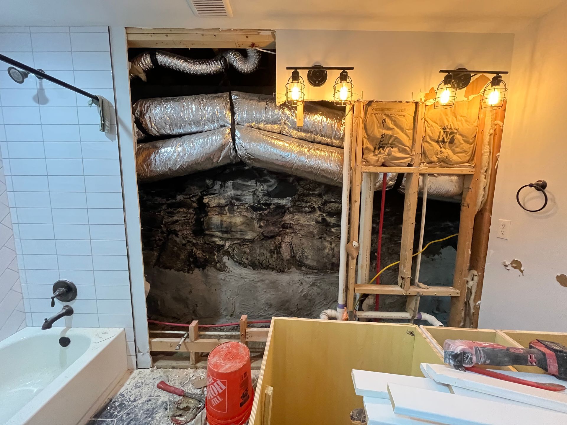 Bathroom under renovation with exposed insulation and plumbing behind a bathtub wall.