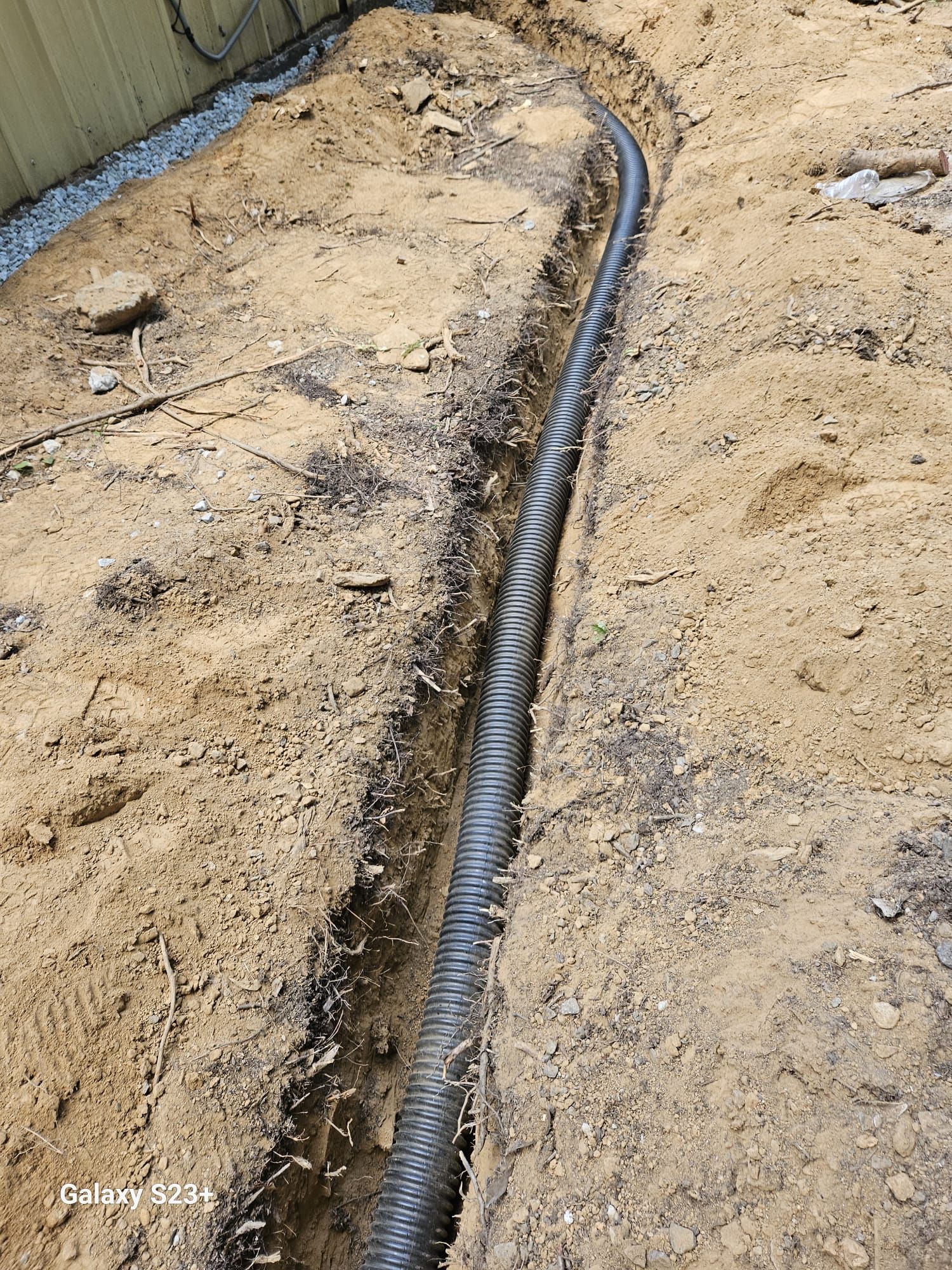 Trenched black pipe laid in a sandy construction site, curving along the ground.