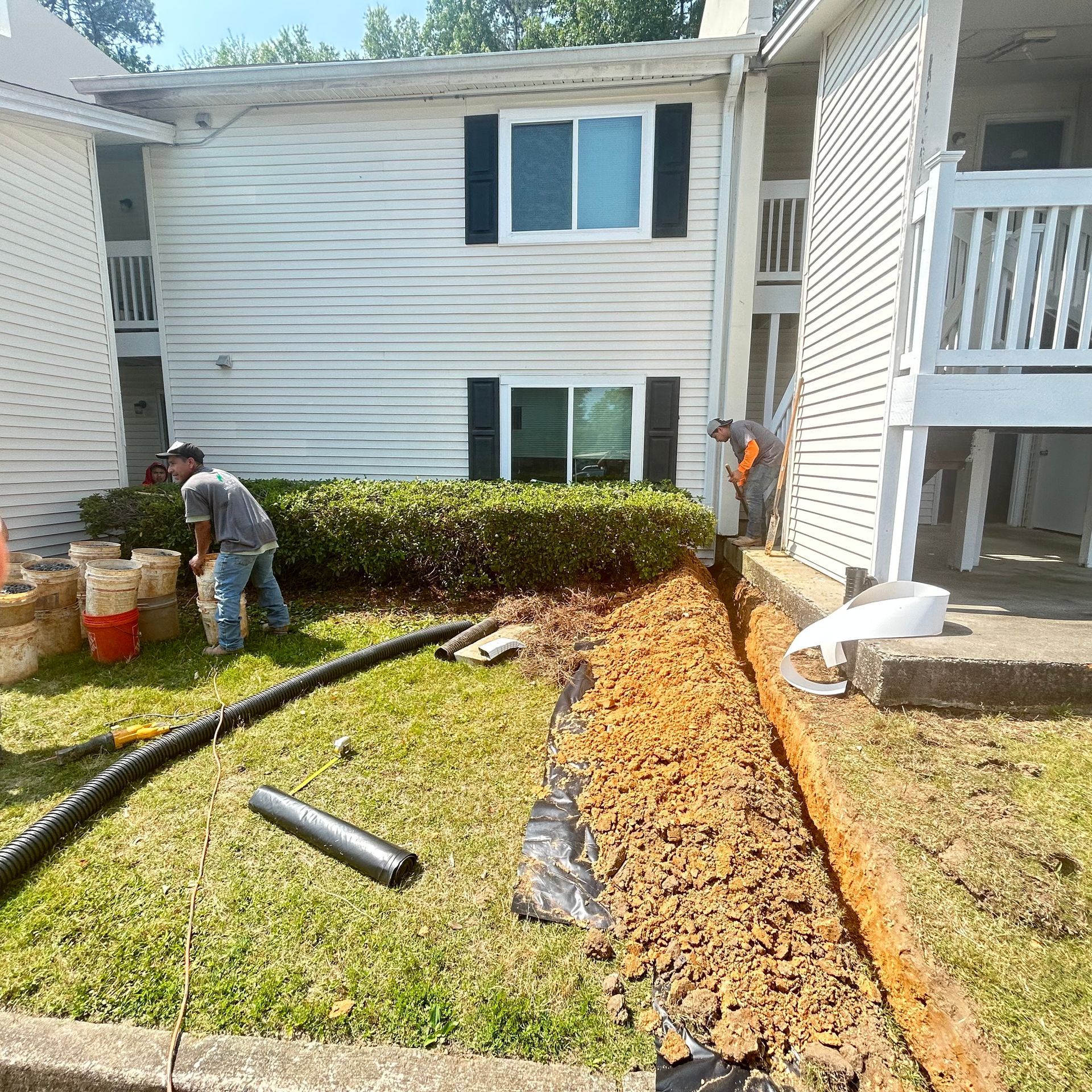 Workers installing a mulch border along a hedge beside an apartment building