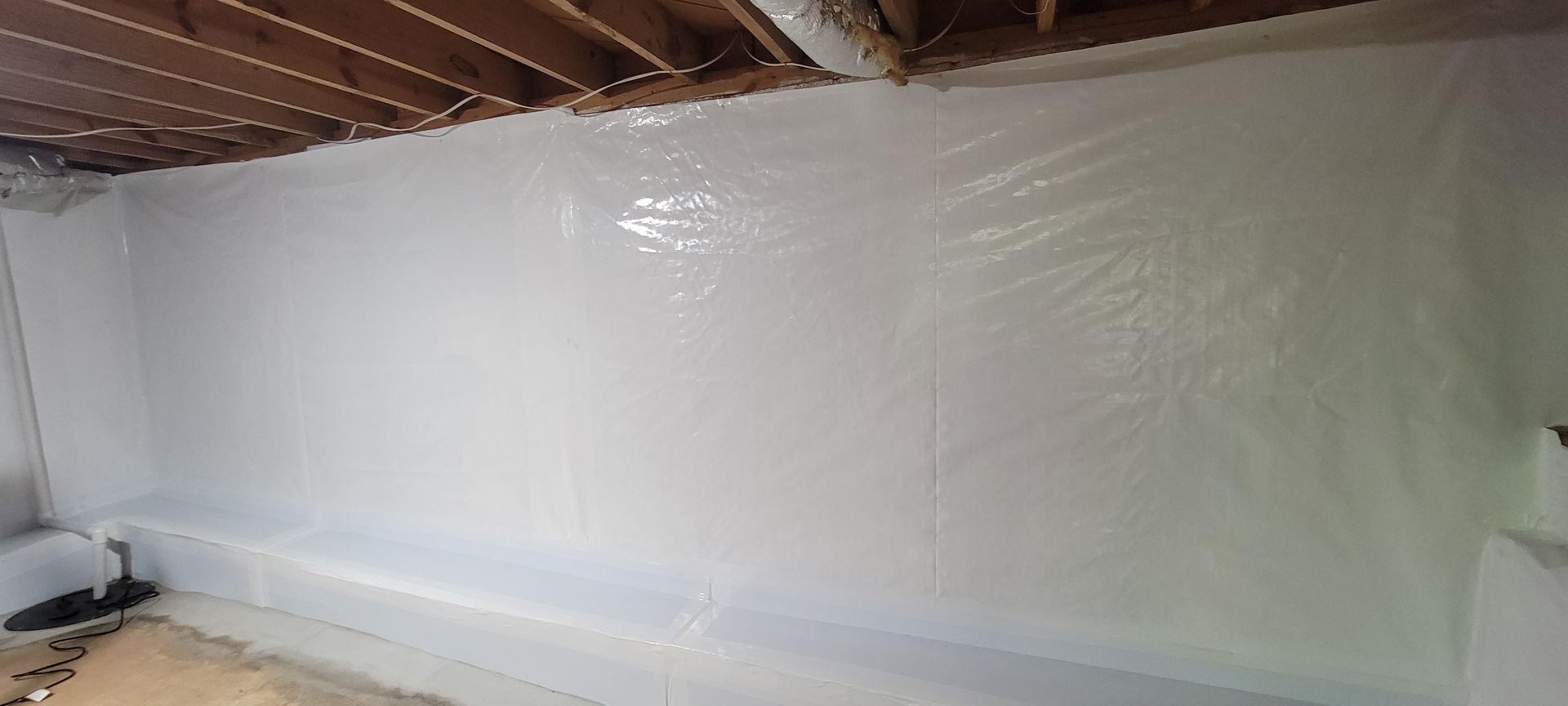 Plastic sheeting covers a wall in an unfinished room with exposed wooden beams and floorboards.
