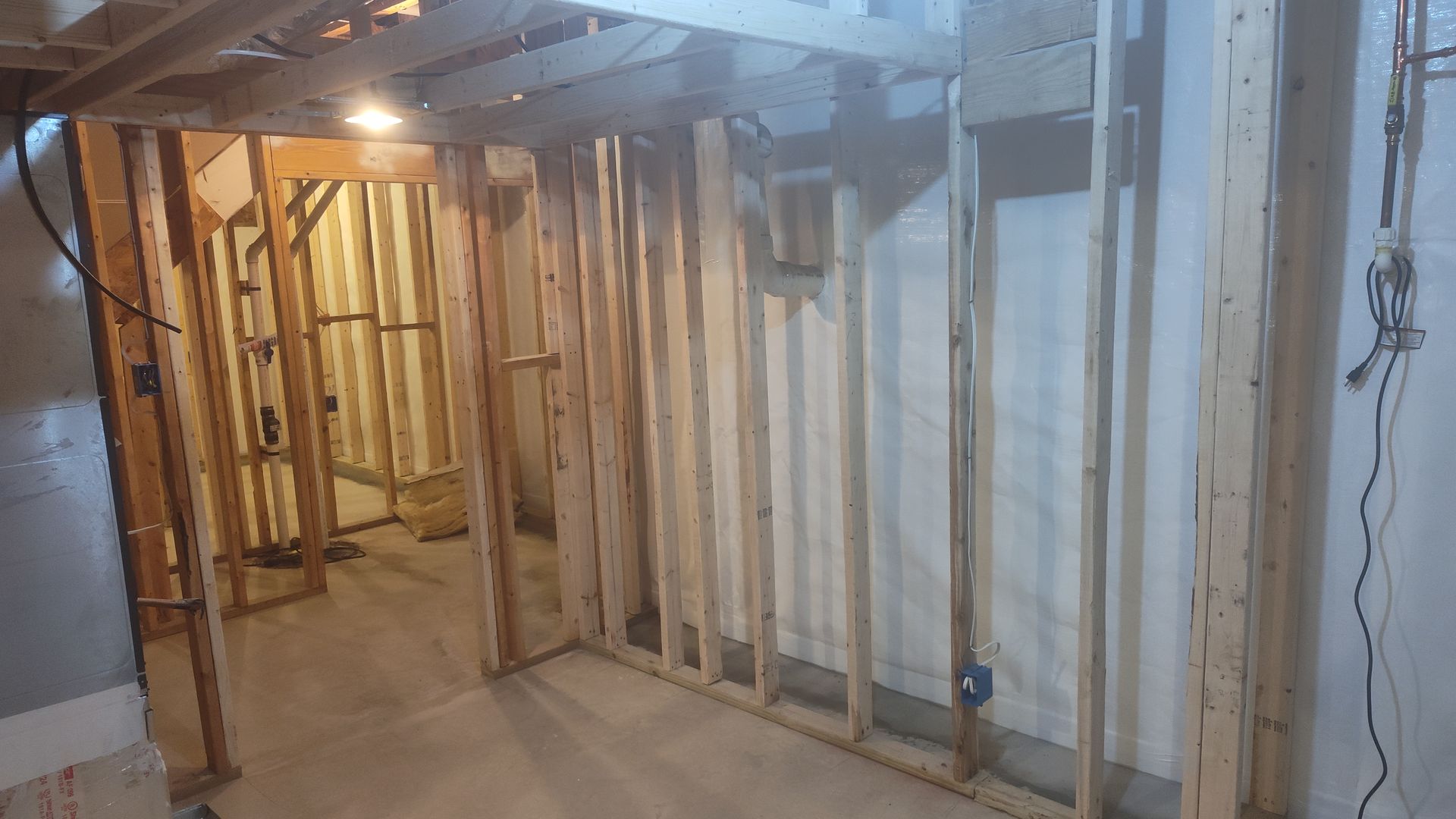 Basement renovation with exposed wooden studs, ceiling beams, and unfinished walls.