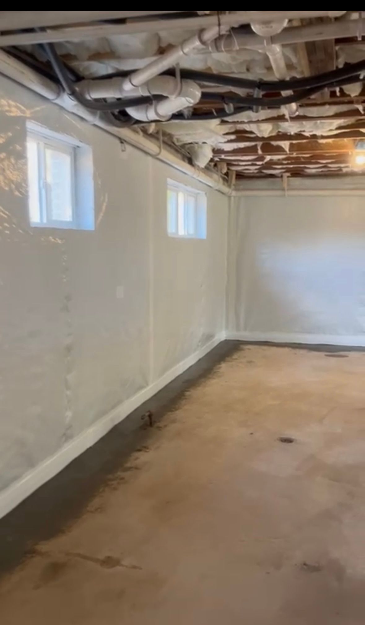 Basement room under renovation with exposed ceiling pipes, white walls, and concrete floor