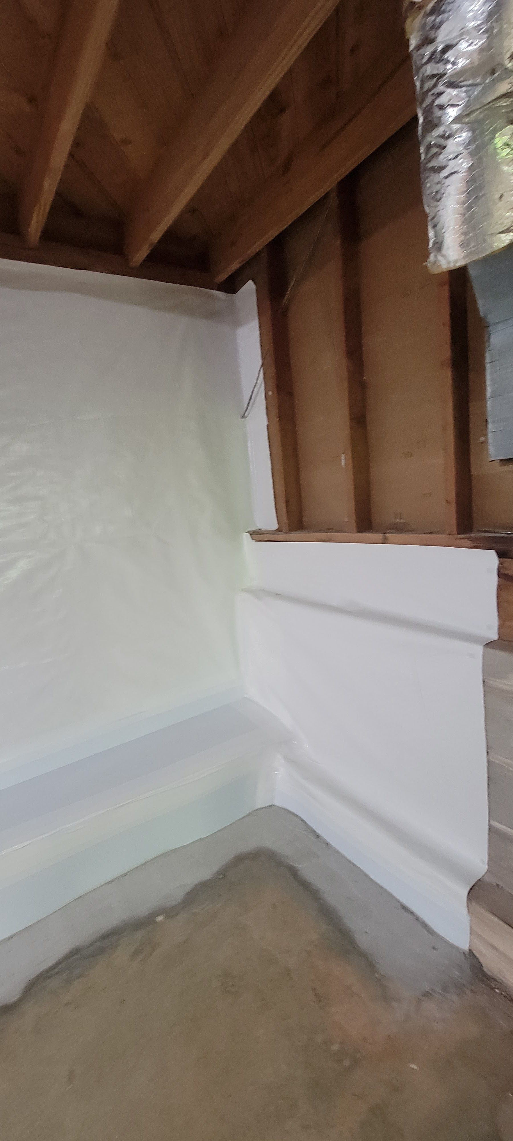 Unfinished basement corner with exposed wooden beams, insulation, and white wall panels