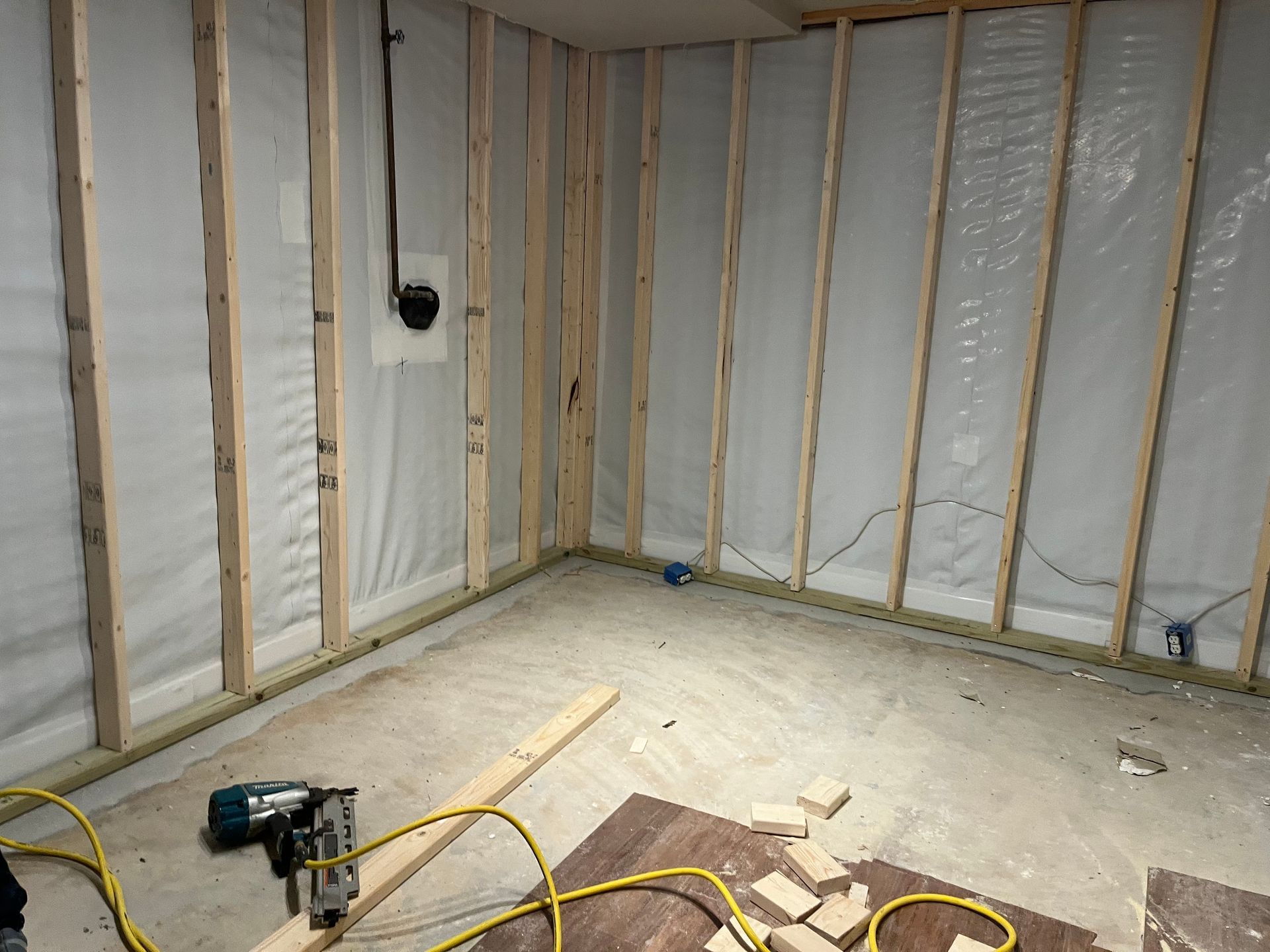 Unfinished room with exposed wall studs, insulation, concrete floor, and a drill on the floor.