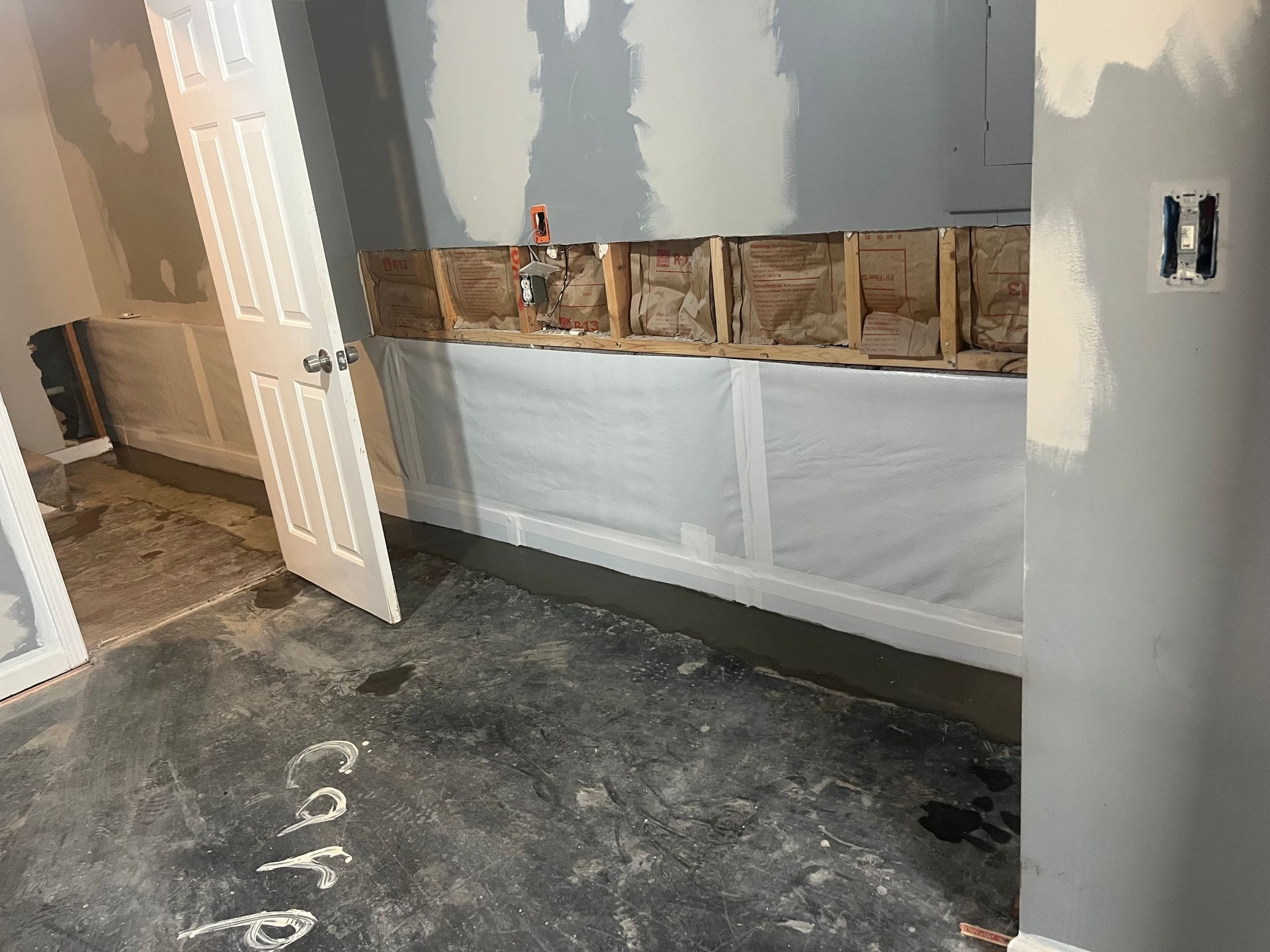 Partially renovated room with exposed wall framing, white drywall, and dusty concrete floor