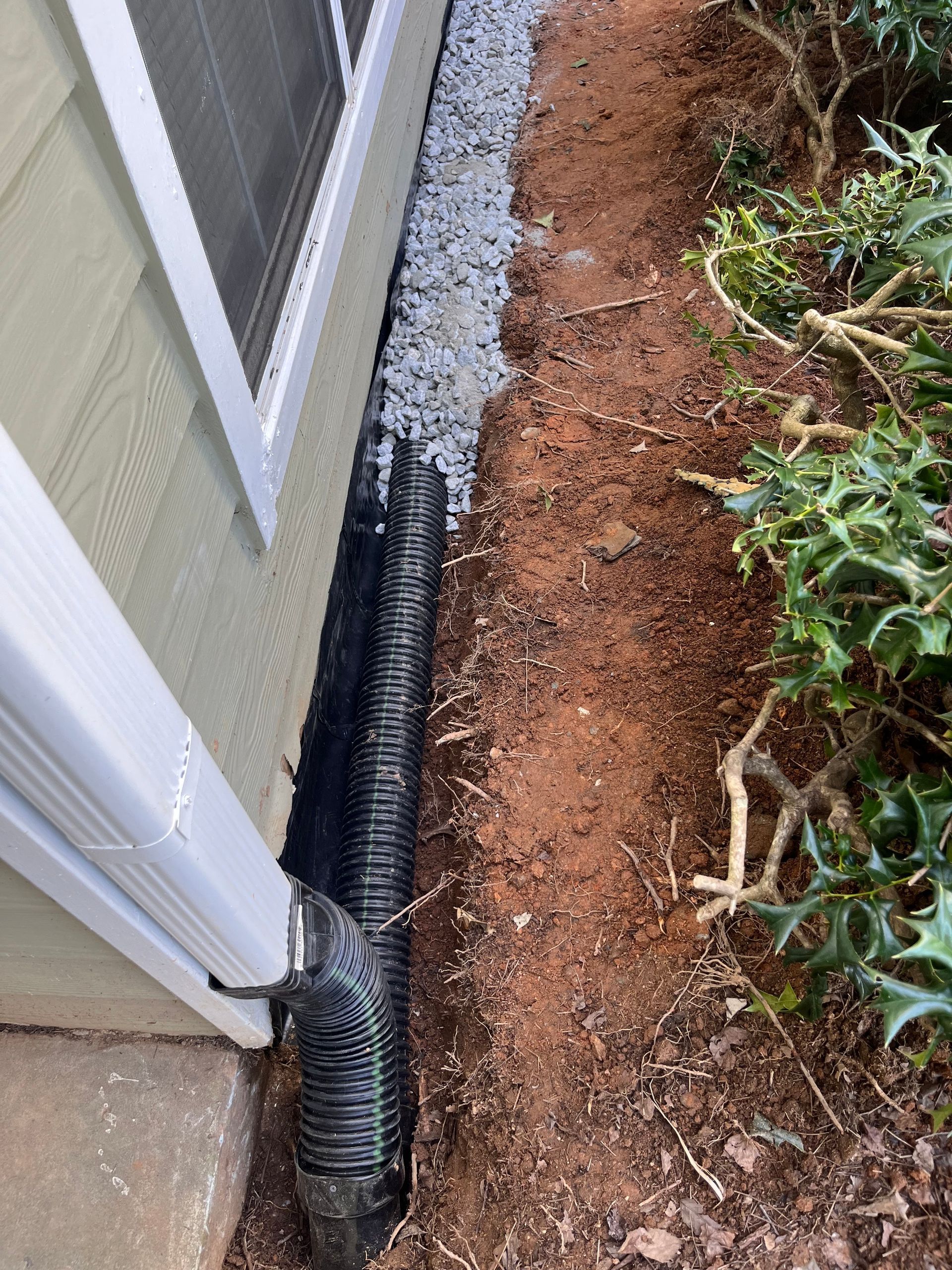 Downspout drain extension along a house foundation beside gravel and dirt landscaping.