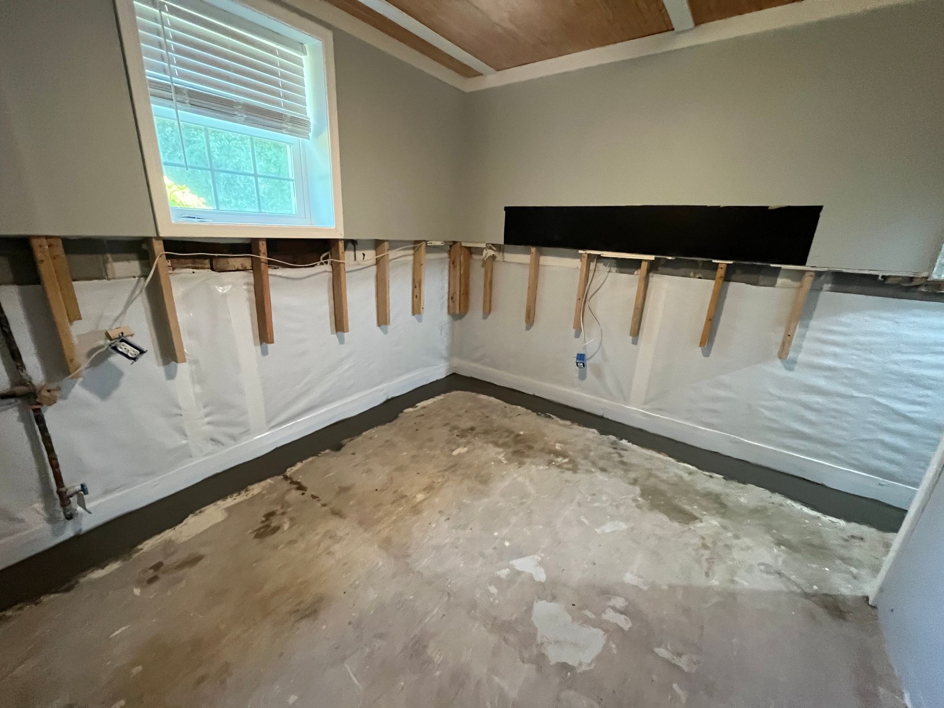 Empty room under renovation with exposed wall studs, window, and concrete floor