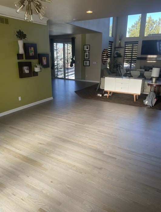 Spacious living room with hardwood floors and green accent wall. A white cabinet and large windows are visible.