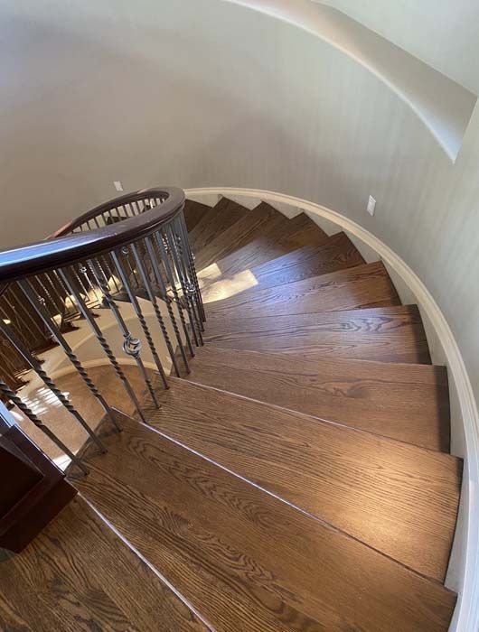 Curved wooden staircase with dark railing, leading upward.