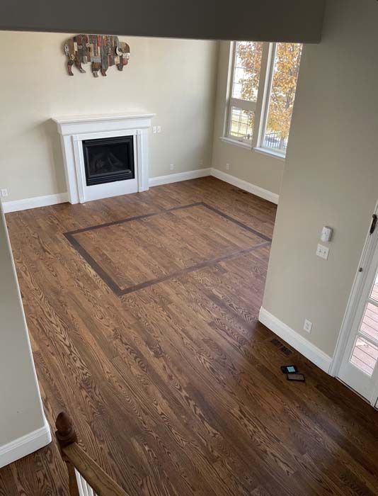 Hardwood floor in room with fireplace and window. Dark stained square border on floor.