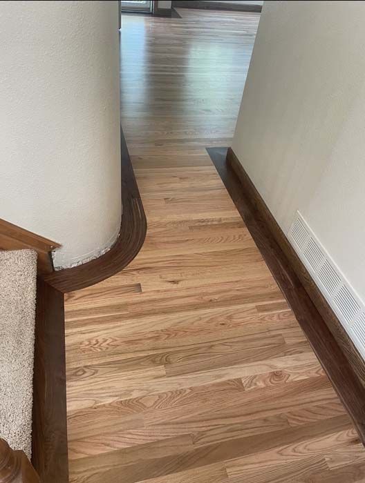 Hardwood floor hallway with dark border, next to a curved white wall.