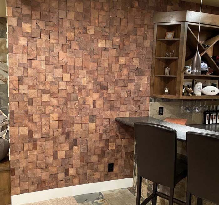 Wooden block wall in a home bar with stools, shelves, and a countertop.