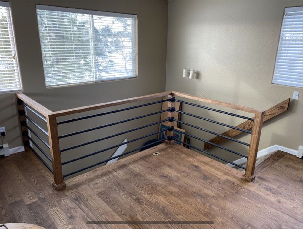Wooden railing with black bars on a second-floor landing with windows.
