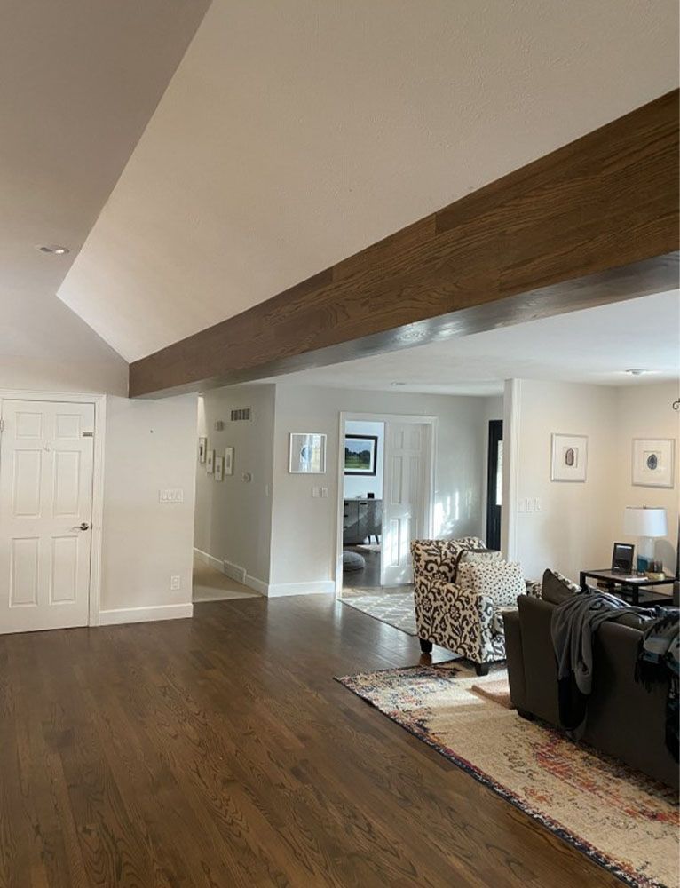 Open-concept living space with dark wood floors, white walls, and a large wooden beam.