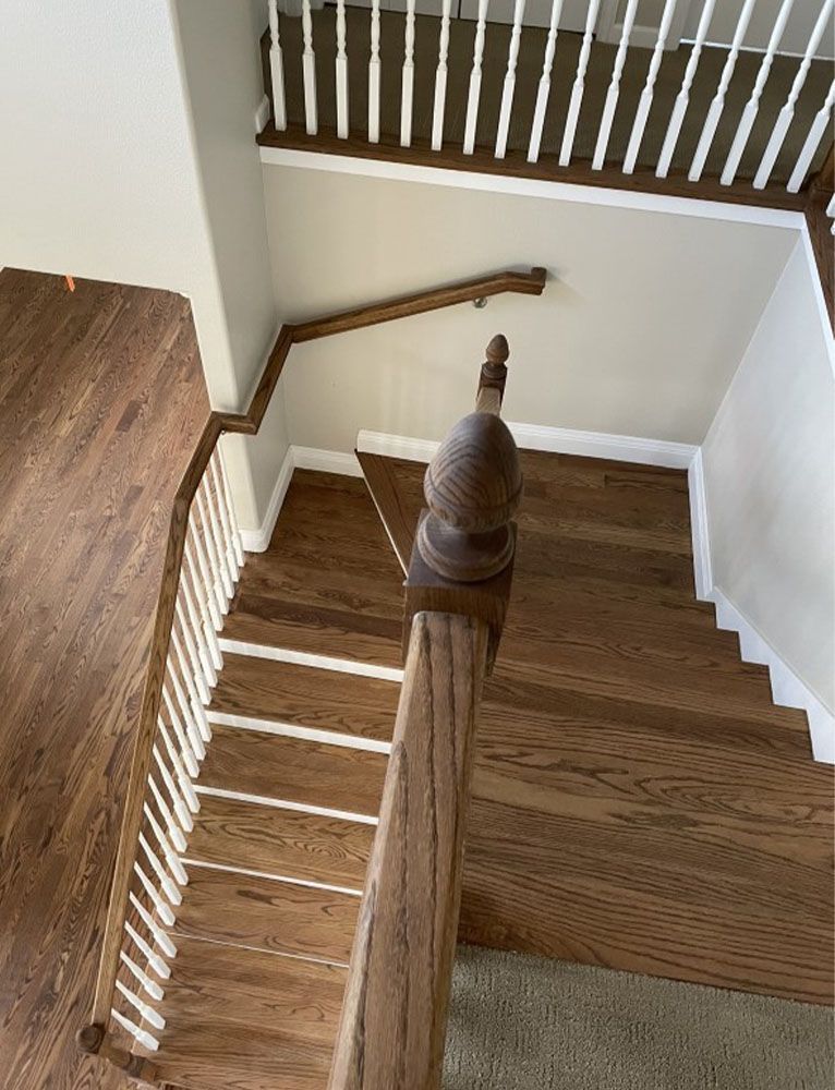 Wooden staircase with white spindles and a brown handrail, viewed from above.