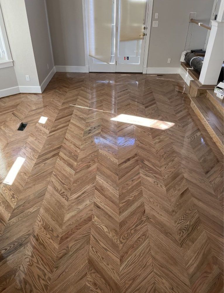 Herringbone patterned wooden floor in a light-filled room. French doors and stairs are visible.