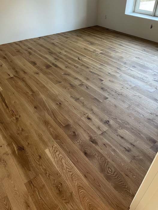 Wooden plank flooring in a room with a window and white walls.