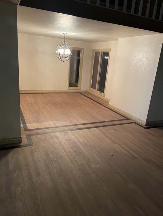 Spacious room with dark wood floors, light walls, and a chandelier. Glass doors and a wooden trim are visible.