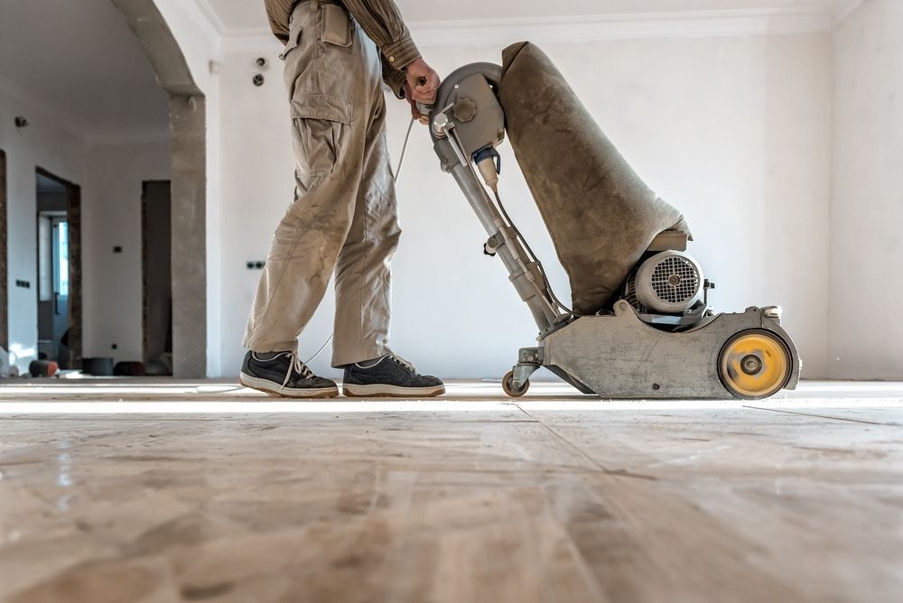 Person sanding a wooden floor with a large machine in a room.