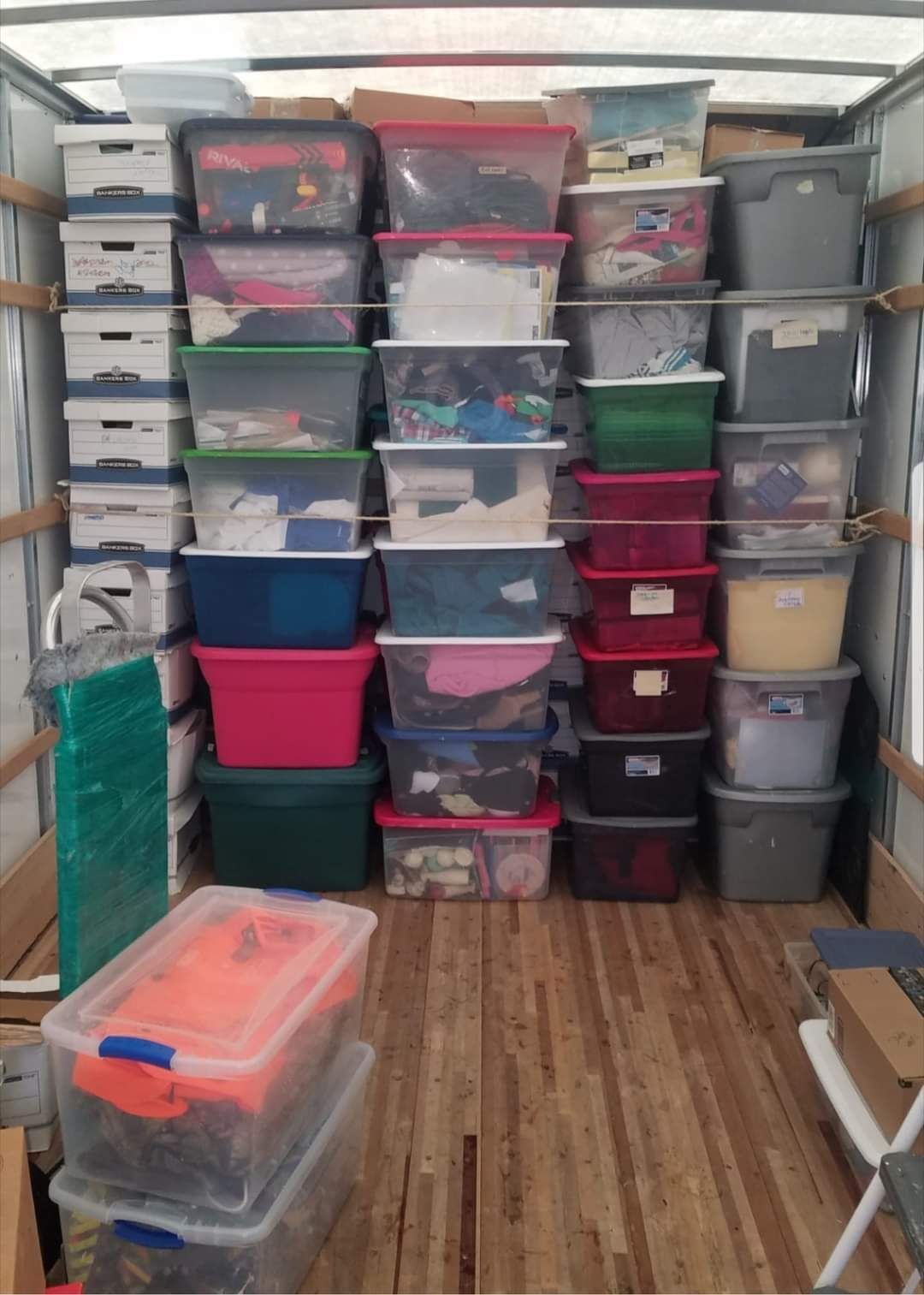 Stacked plastic storage bins of various colors packed in a small trailer or storage space.