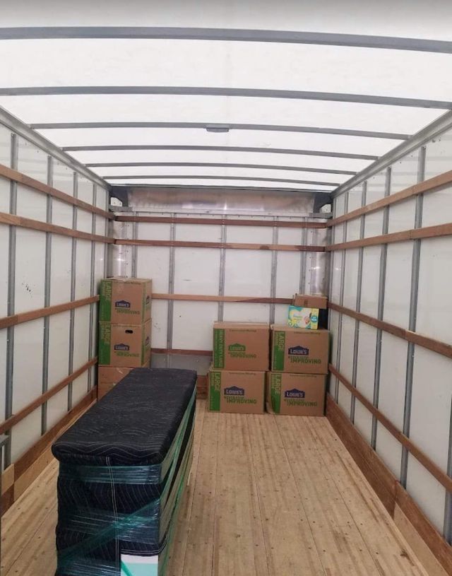 Empty moving truck with stacked cardboard boxes and a wrapped mattress inside.