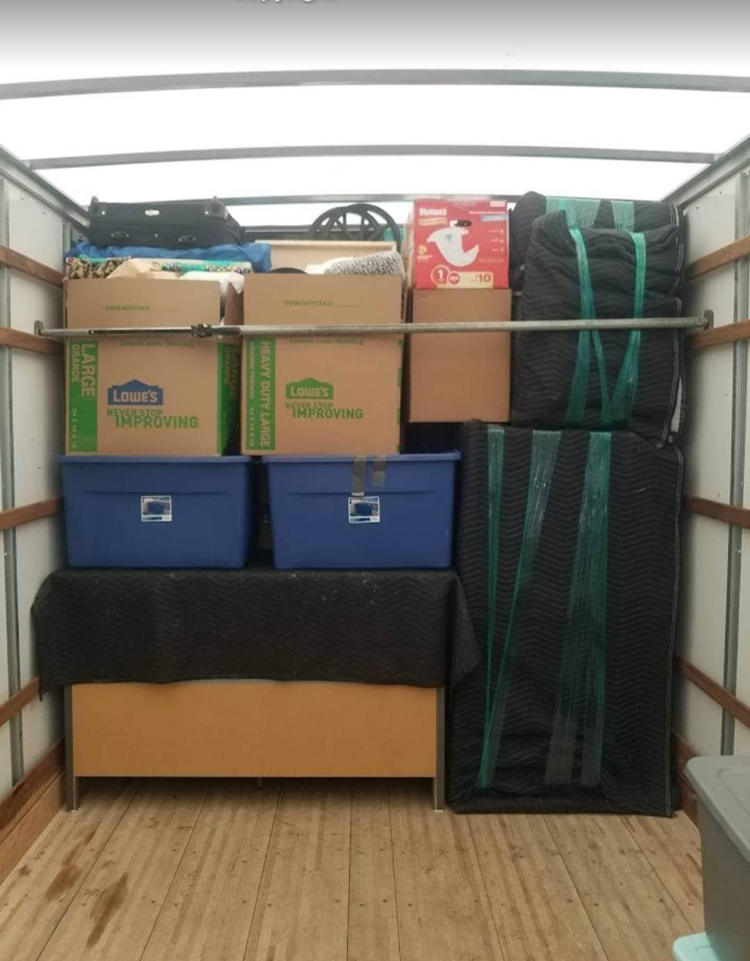 Packed moving truck with stacked boxes, blue bins, and a tall black item strapped on the right side.