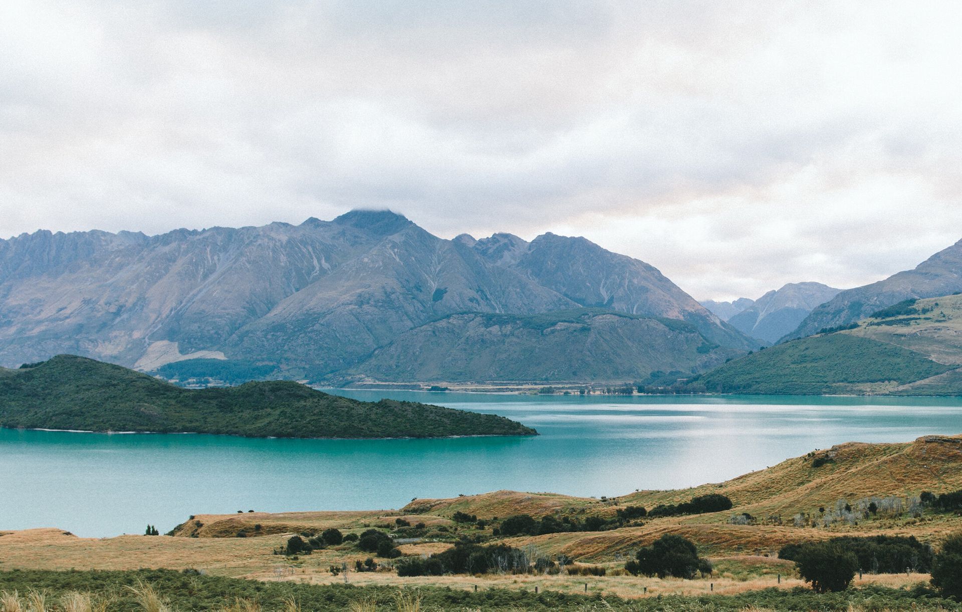 Turquoise lake with mountains under a cloudy sky and grassy shoreline in the foreground