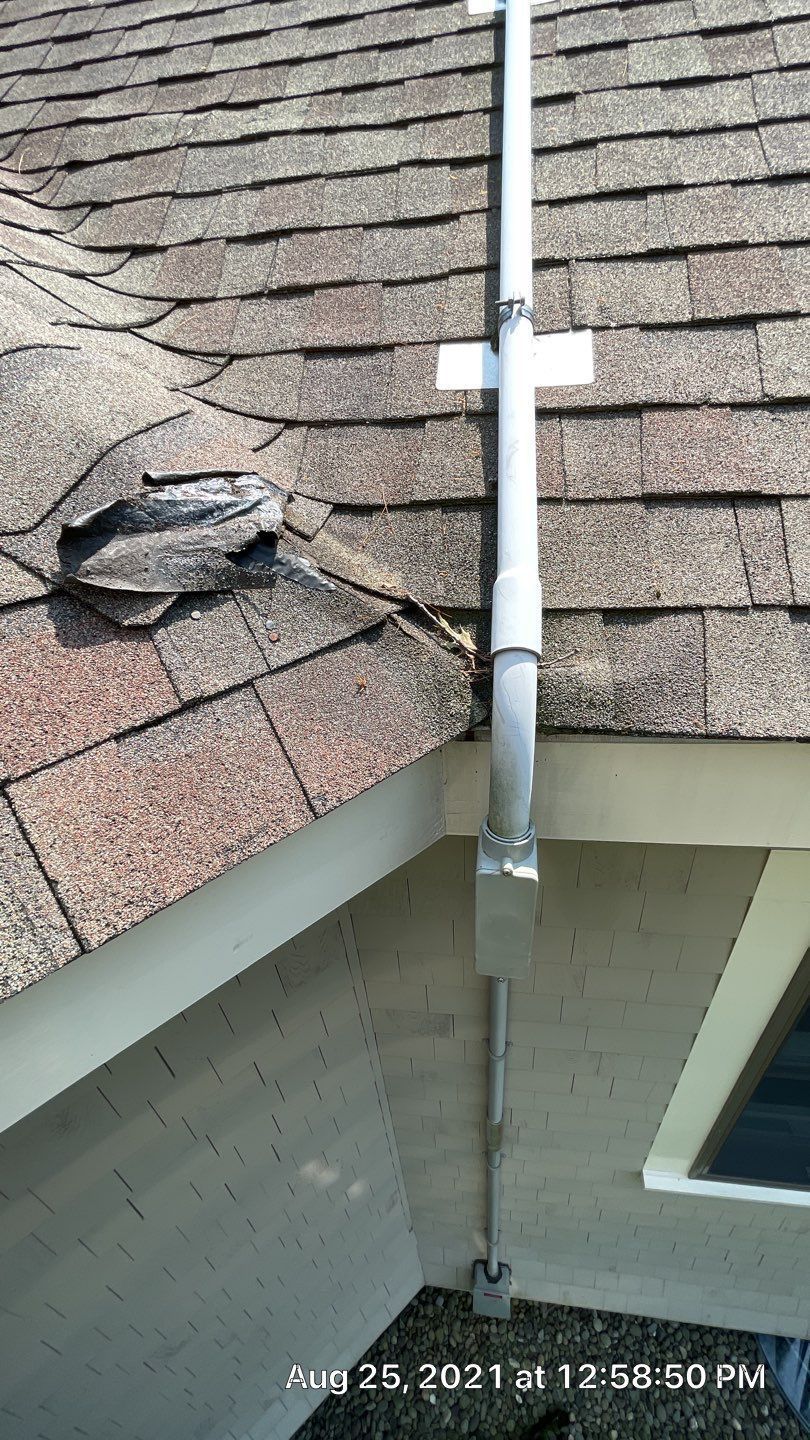A PVC conduit runs up a shingled roof, transitioning to metal piping that descends along the exterior wall of a building.