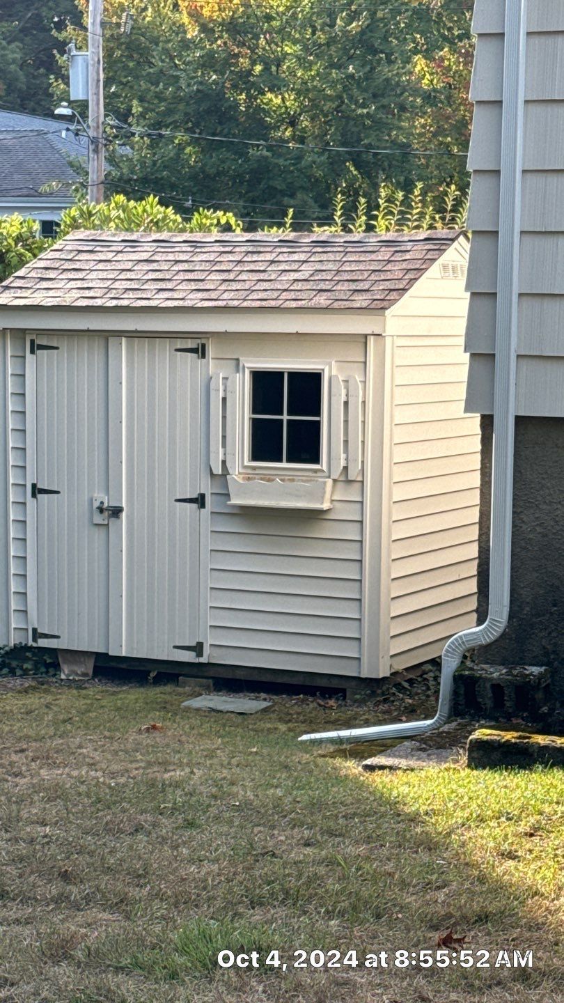 A white shed with a window in the backyard of a house.