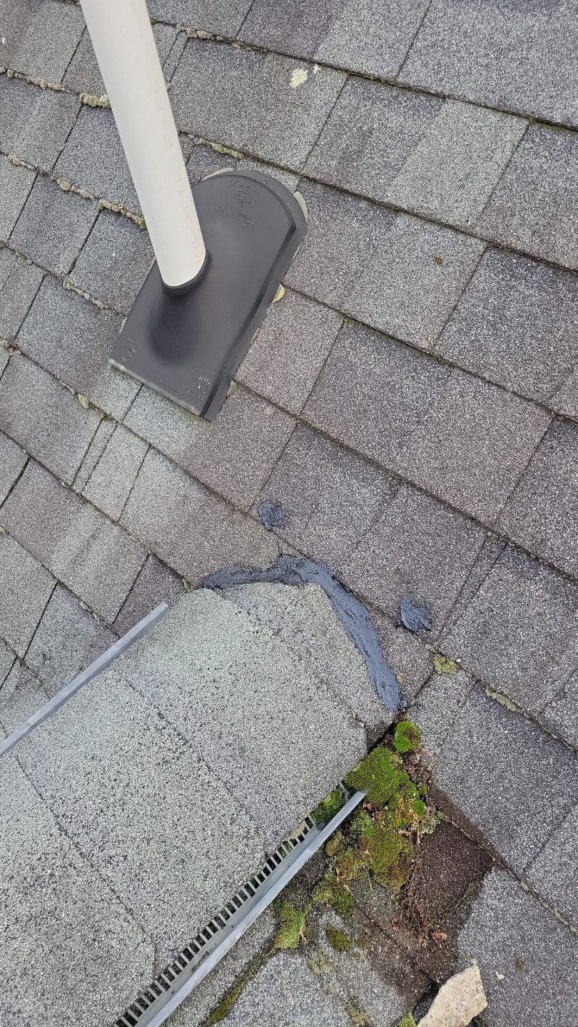 Roof with a vent pipe and visible damage near the edge, with algae growth.