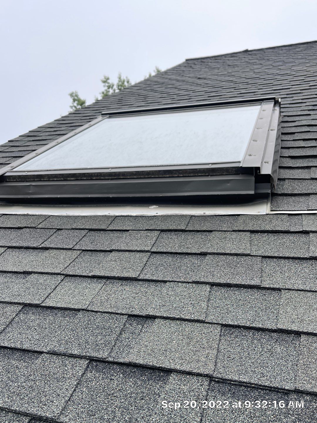 Skylight on a shingled roof, set against a cloudy sky.