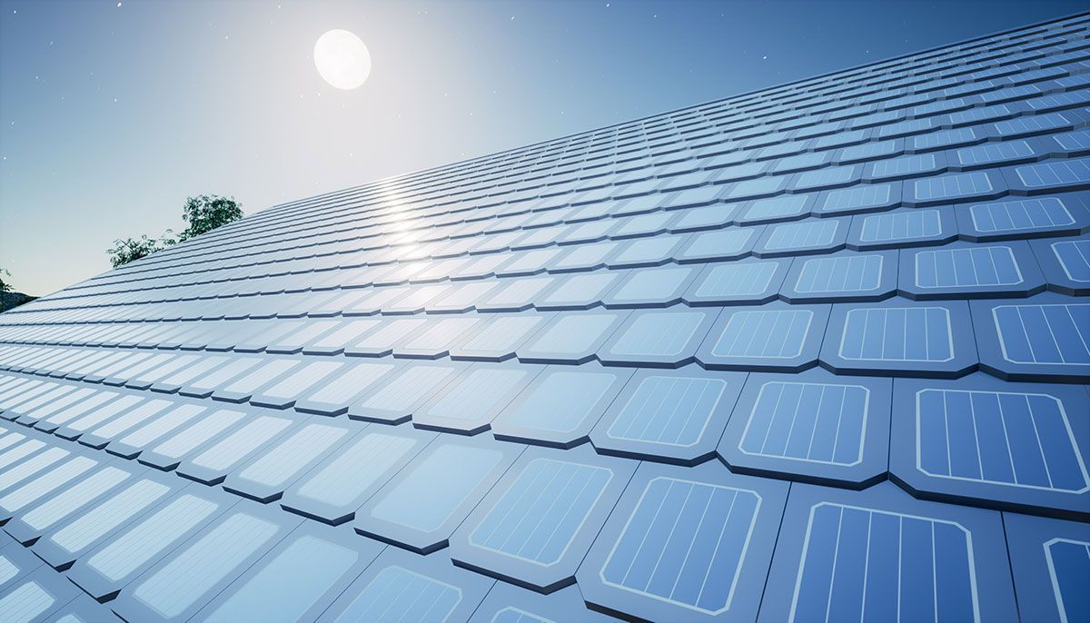 Solar roof tiles under a bright sun against a blue sky, reflecting light.