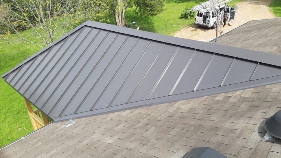 Gray metal roof section on a house, contrasting with an asphalt shingle roof.
