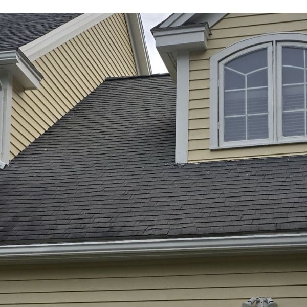 Yellow house with dark gray shingle roof and white trim, close-up view.