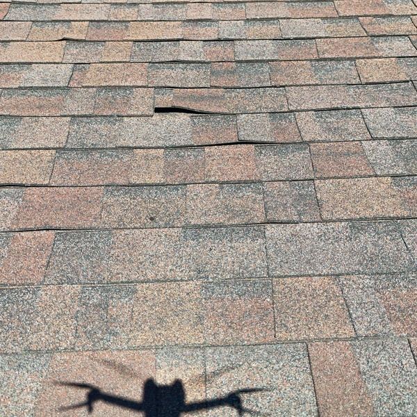 Shingles lifted by nail pop-through on aging roof