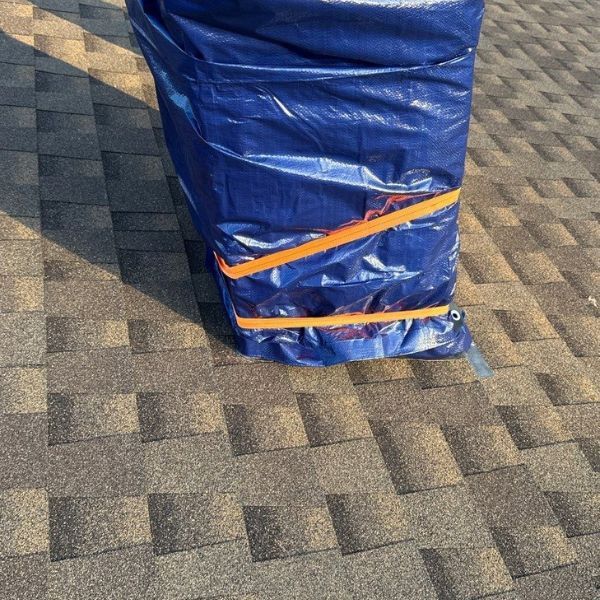 Blue tarp secured with orange straps on a brown shingle roof.
