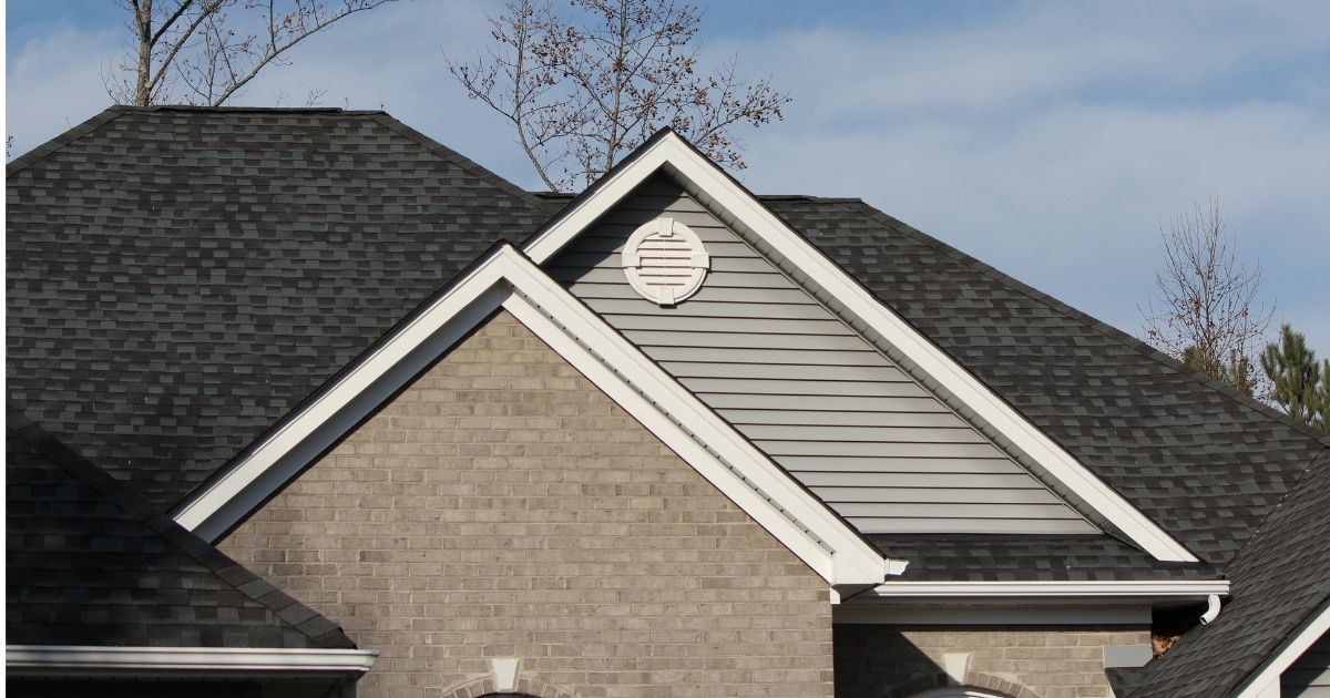 Gray asphalt shingle roof with a white-trimmed gable end, light brown brick facade.