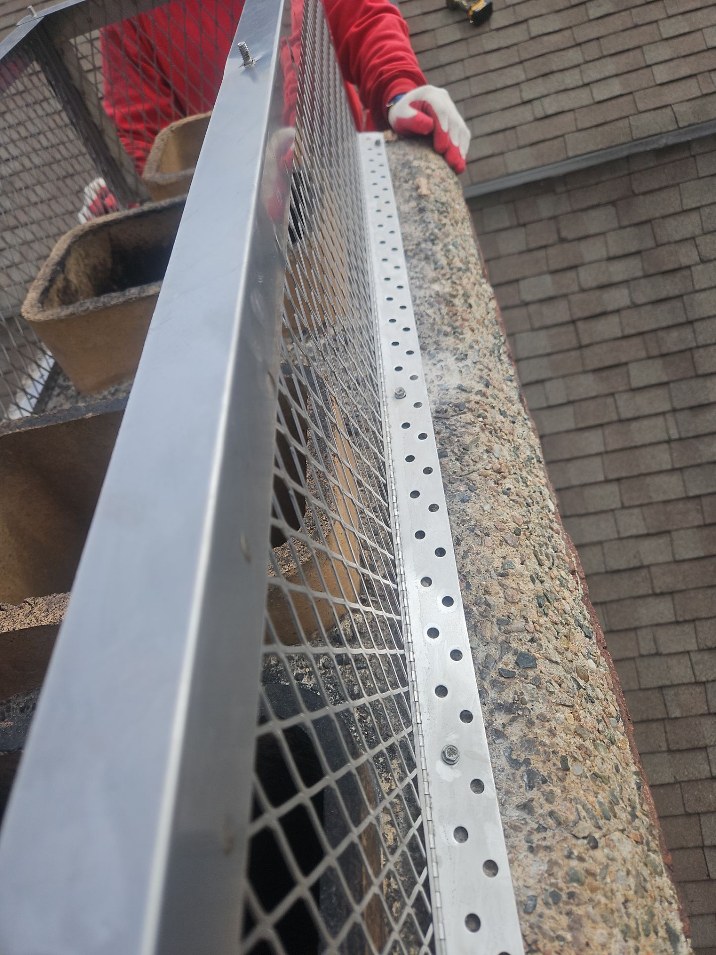 Worker installing wire mesh along a chimney. They are wearing red and white gloves.