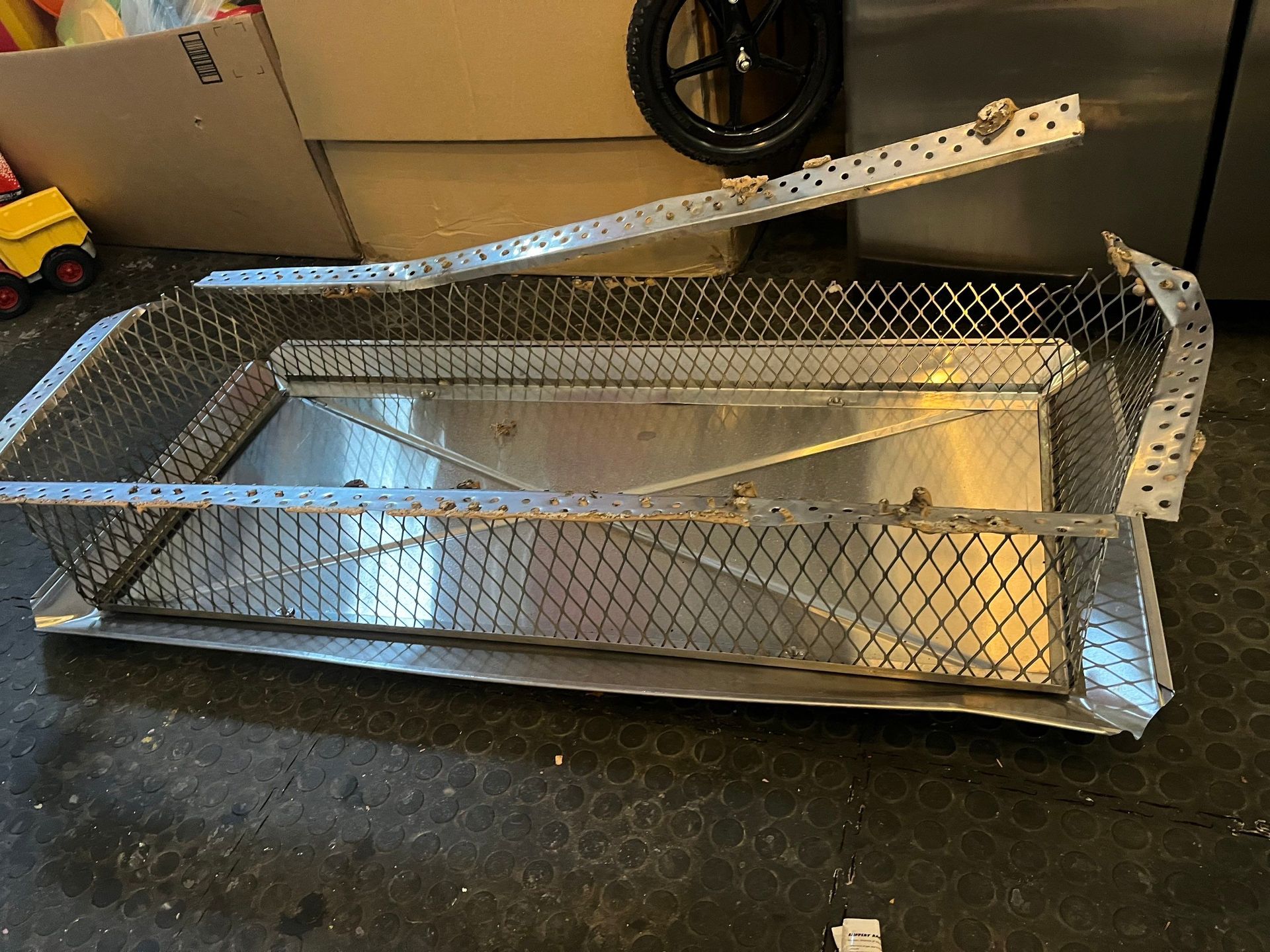 Metal sifting box with a mesh basket, tray, and hinged handle; resting on a dark surface.