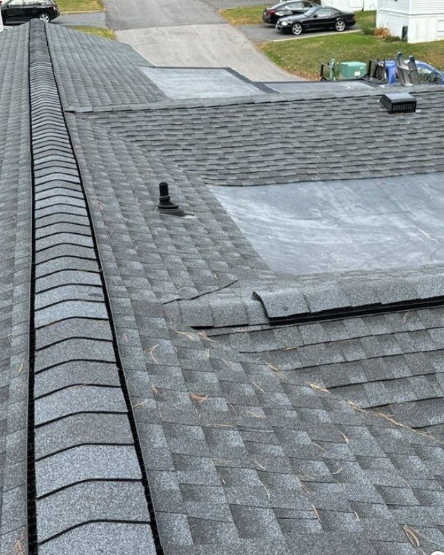View of a gray shingled roof with a dark flat section and a street in the background.