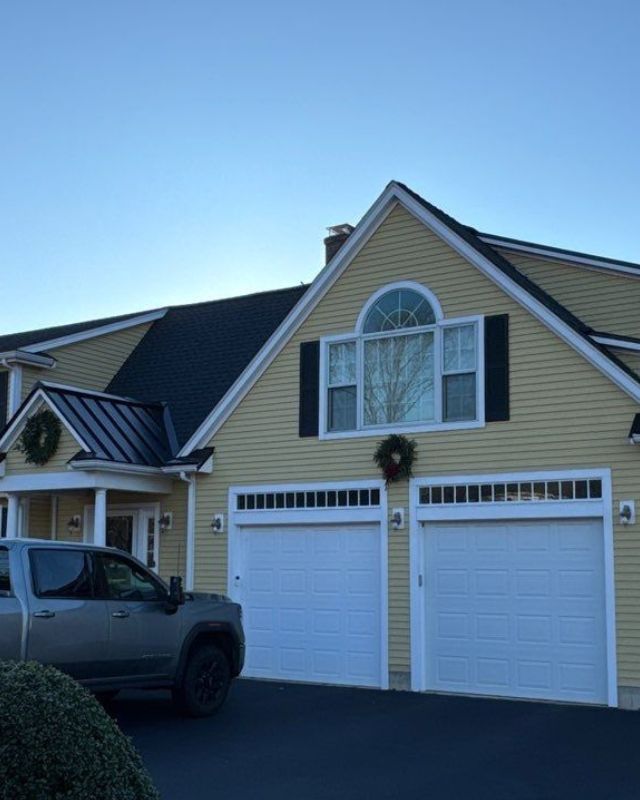 Yellow house with black roof, two-car garage, and gray truck in driveway under a clear blue sky.
