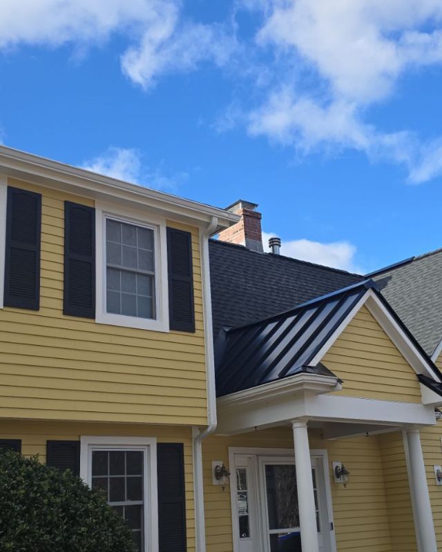 Yellow house with black shutters, roof, and blue sky.