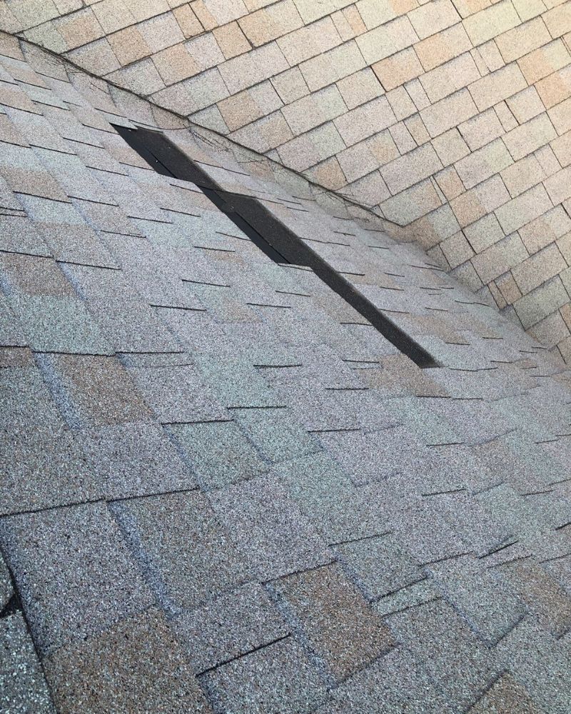 Roof with a long, dark opening, possibly for ventilation or an antenna. Shingles are in shades of gray and brown.