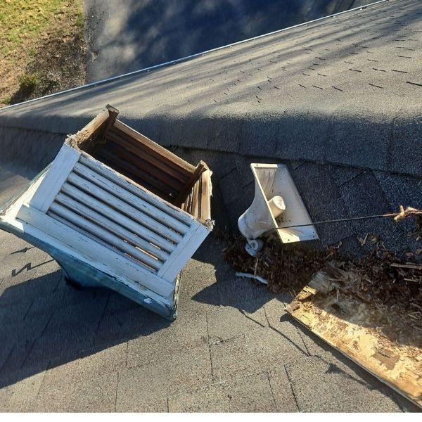 A damaged white roof vent and a detached speaker component lying on an asphalt shingle roof among scattered leaves.