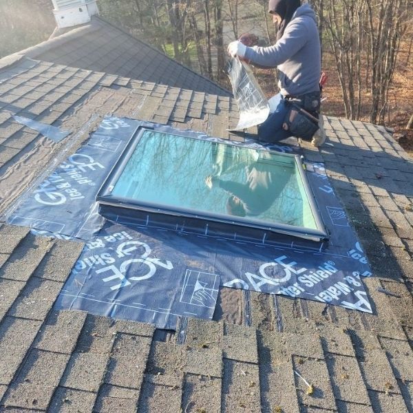 A worker installs a skylight on a residential roof, applying protective waterproof flashing around the frame.