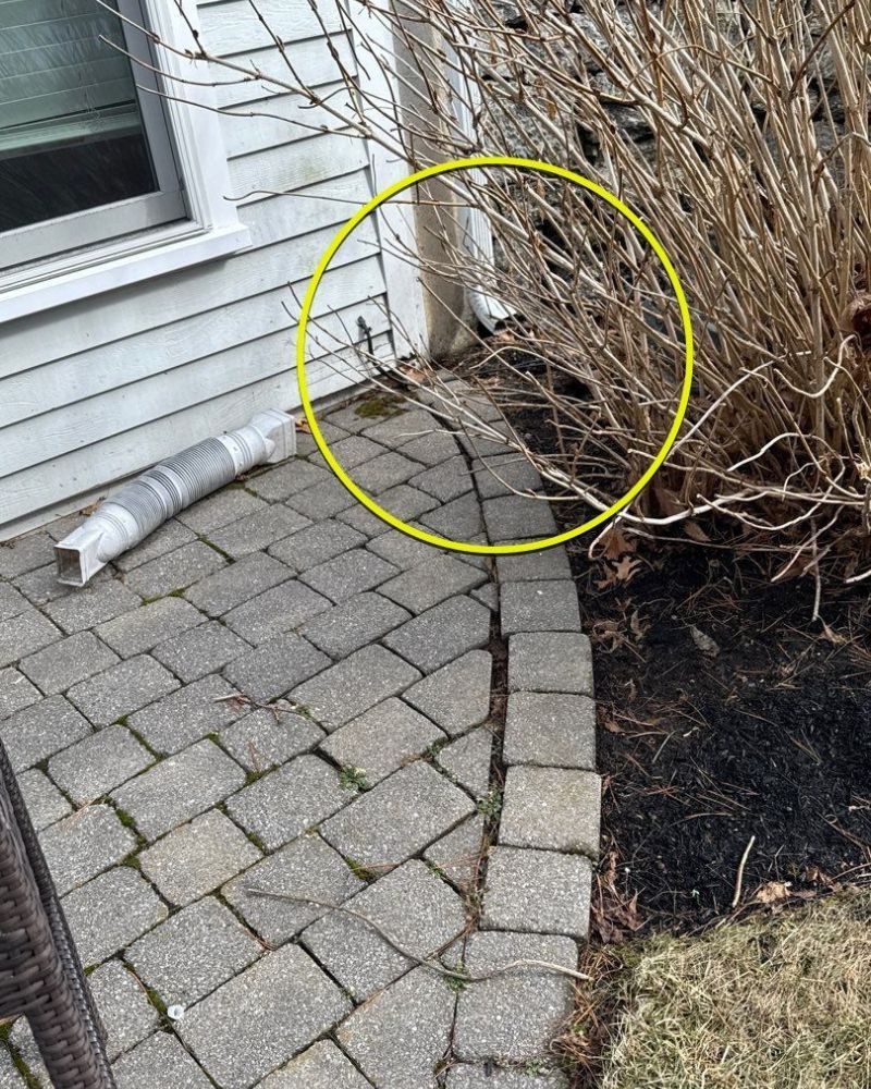 Yellow circle surrounds a downspout area beside a bush. A brick patio is in the foreground.