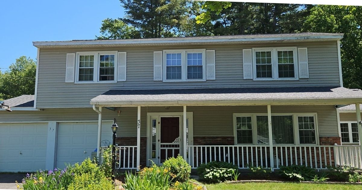 Two story tan home with a front porch and new roof.